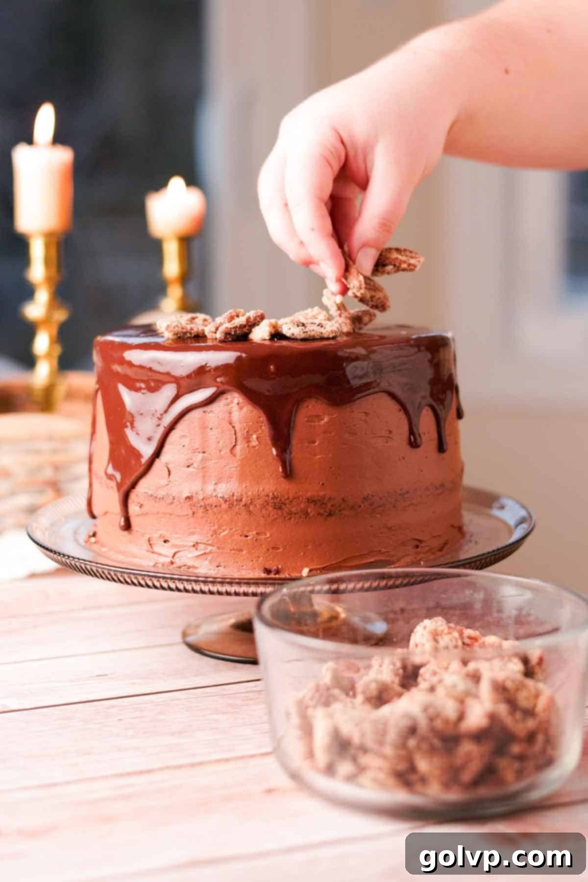 Decorating the top of the chocolate cake with more praline pecans after the chocolate drip has set, adding a final touch of crunch and elegance.