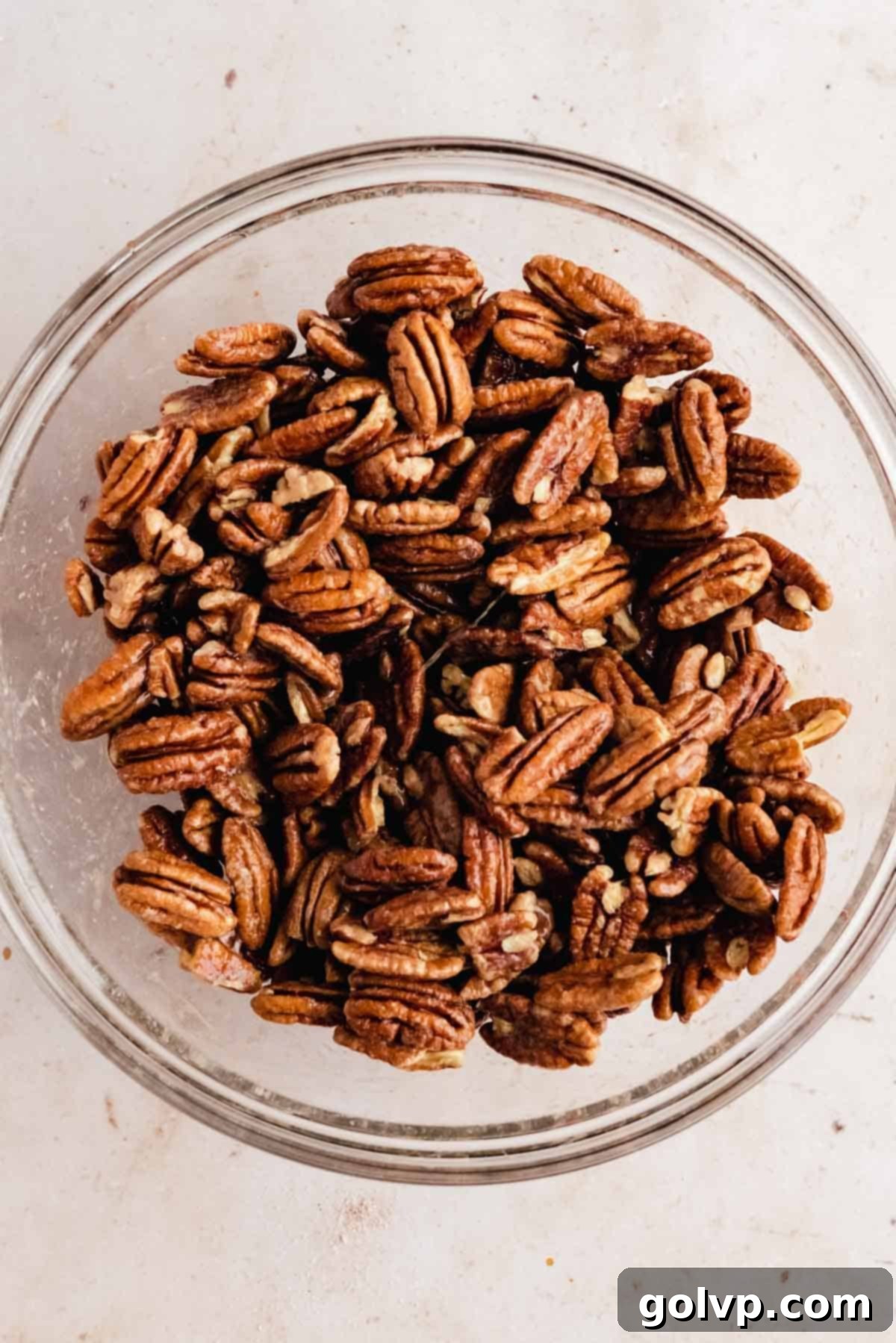 Coating raw pecan halves with whisked egg whites, vanilla, and salt in a clear glass bowl, preparing them for the praline coating.