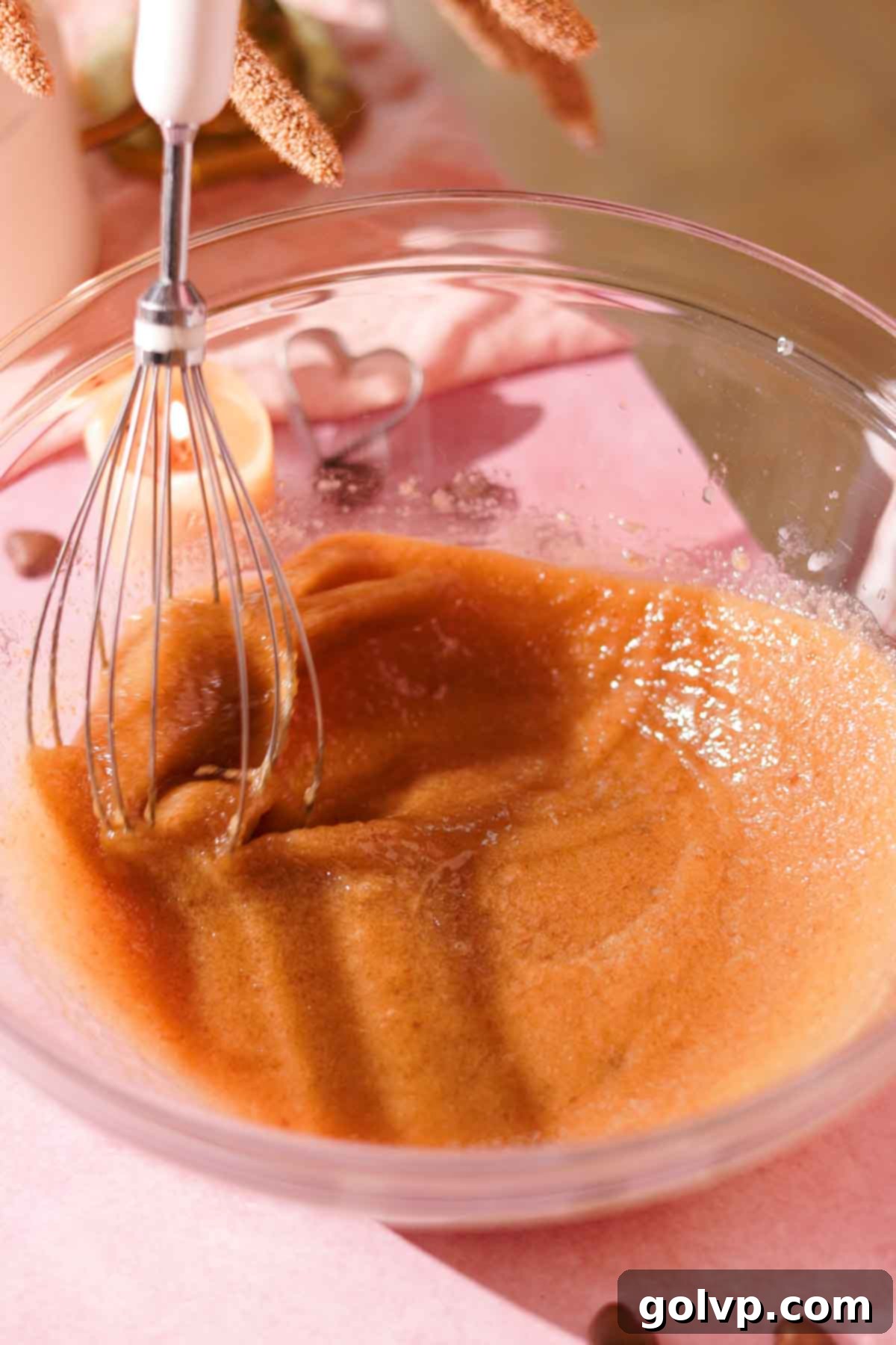A close-up shot of melted butter, brown sugar, granulated sugar, and salt being whisked together in a clear glass bowl, showing the creamy texture forming.