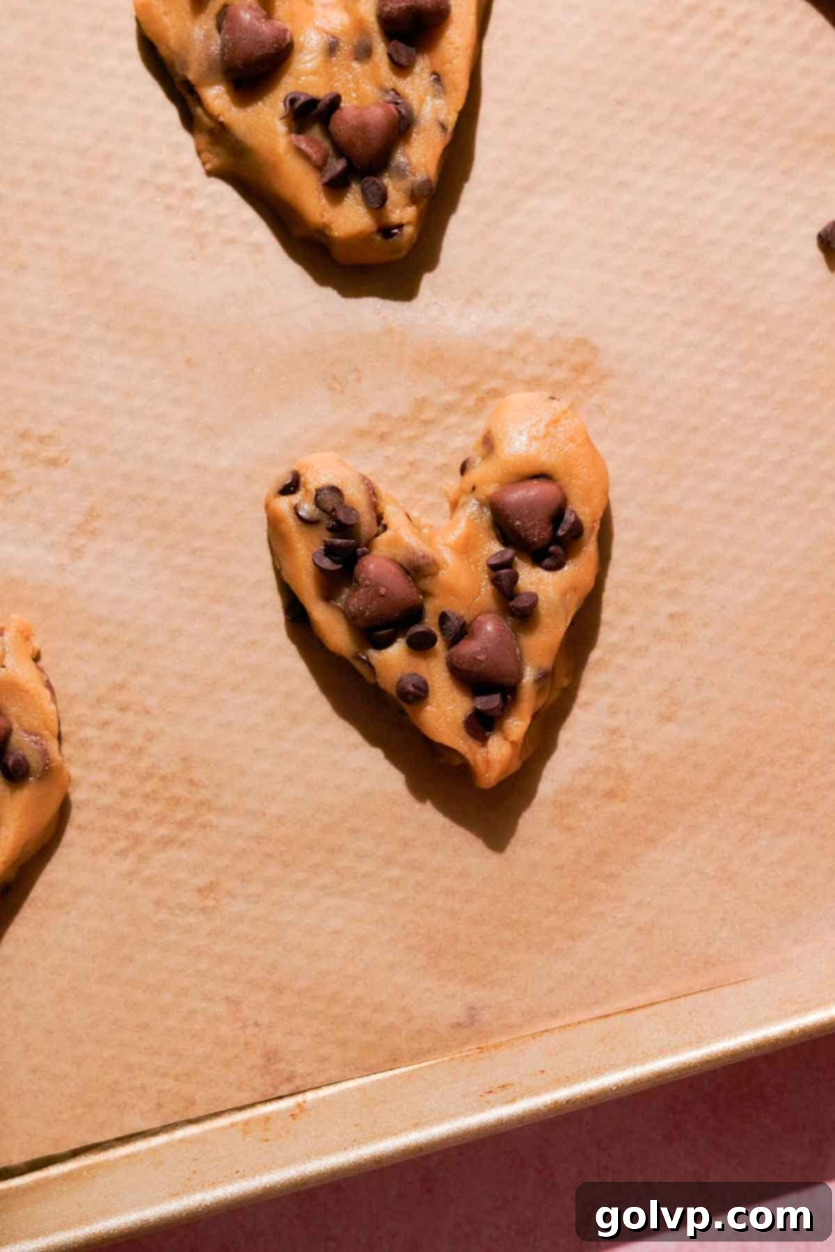 Neatly shaped cookie dough hearts, each topped with a scattering of chocolate chips, arranged on a parchment-lined baking sheet, ready for chilling and baking.