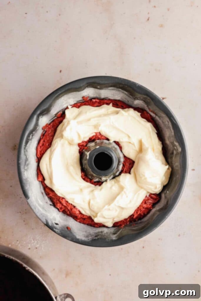 Image depicting the layering of the cream cheese swirl on top of half the red velvet batter in a bundt pan.