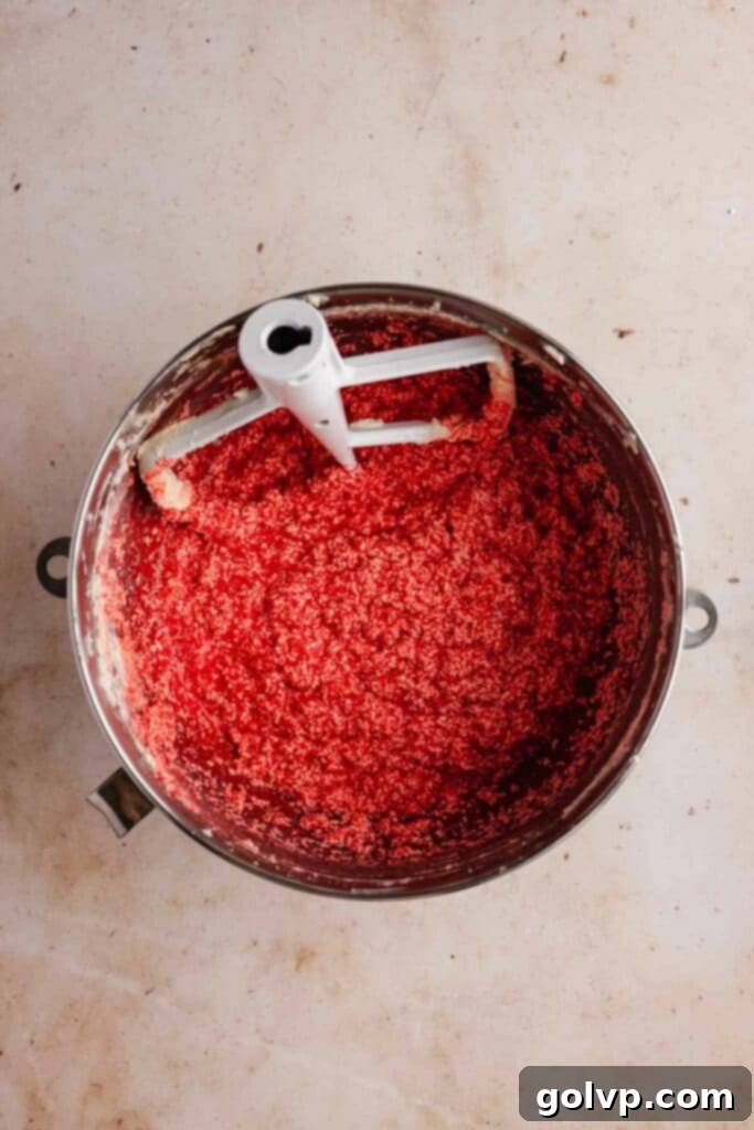 Process photo of adding red food coloring drop by drop to the red velvet cake batter until a vibrant red color is achieved.
