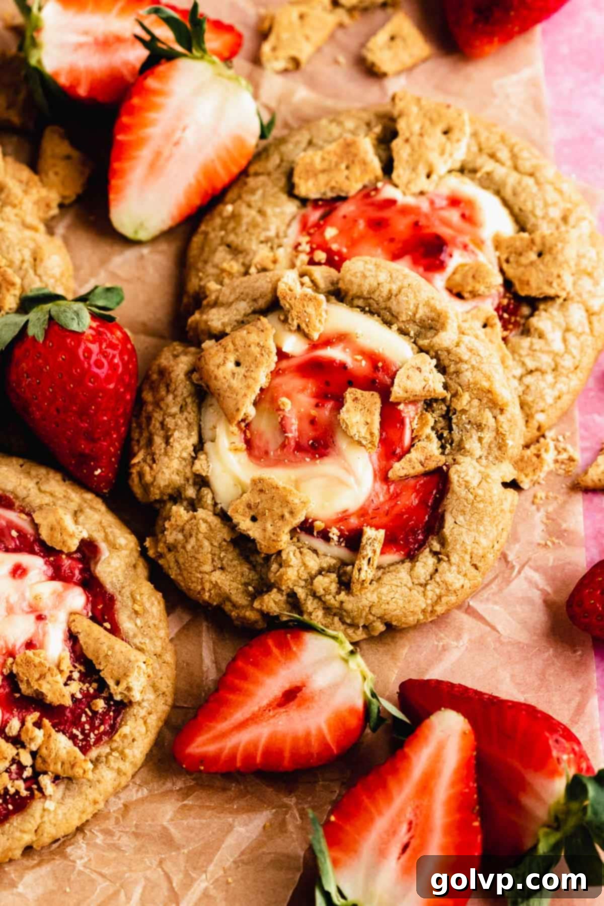 Decadent Strawberry Cheesecake Cookies 2 Freshly baked strawberry cheesecake cookies on a cooling rack, some with a visible gooey center and graham cracker topping
