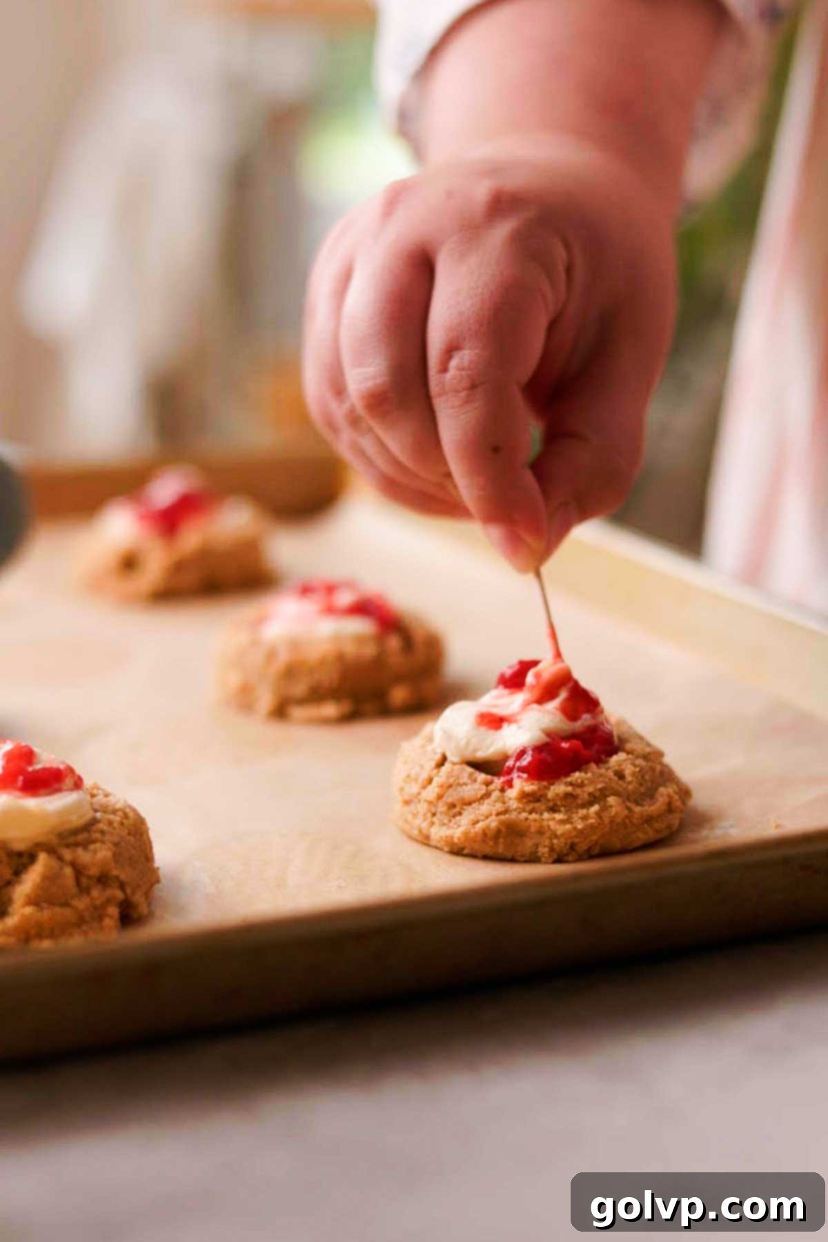 Swirling strawberry sauce into the cheesecake filling within a cookie with a toothpick.