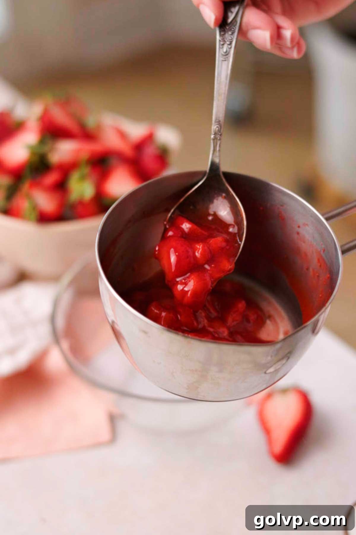 Thickened strawberry sauce being drizzled from a spoon, showing its rich texture.