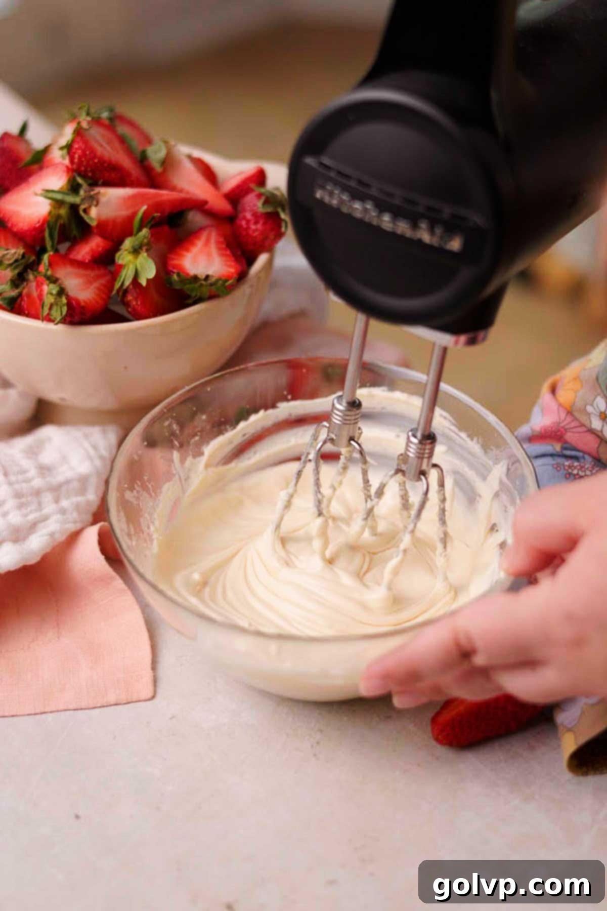 Whisking cream cheese, sugar, vanilla, and egg in a glass bowl to create a smooth cheesecake filling.