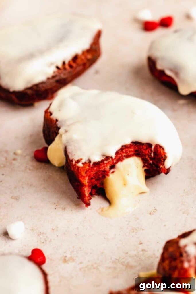 Red velvet heart shaped donut with filling oozing out and cream cheese glaze