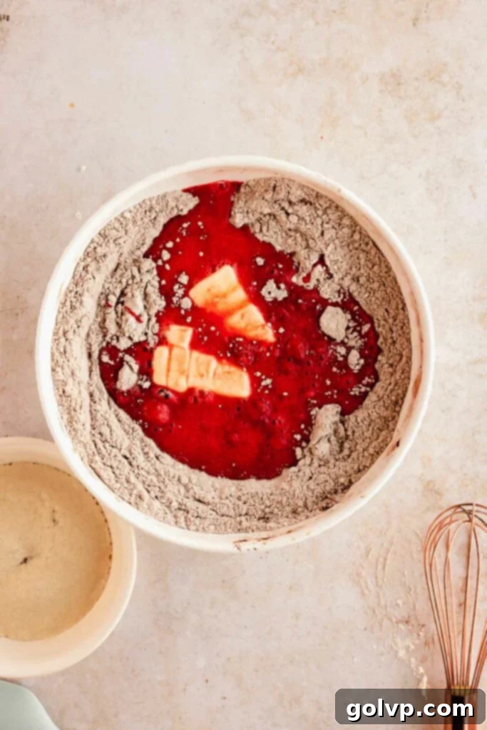 Mixing red velvet fried donut dough by hand in a large bowl, showcasing its rich color and sticky texture.