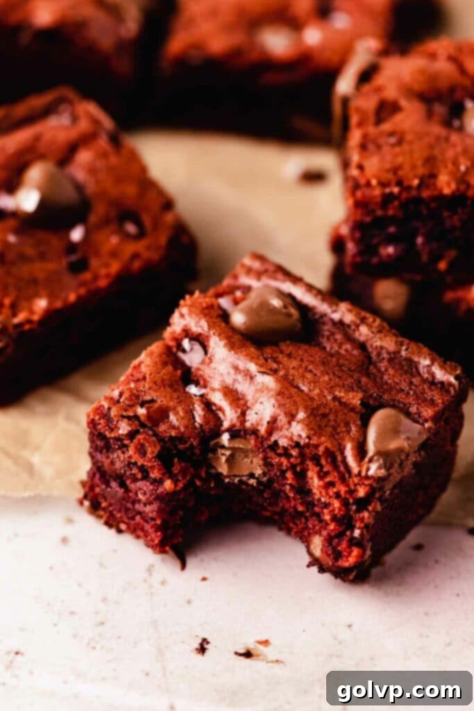 A deliciously fudgy red velvet brownie with a bite taken out, revealing a rich red interior and chocolate chips, adorned with small chocolate hearts for a festive touch.