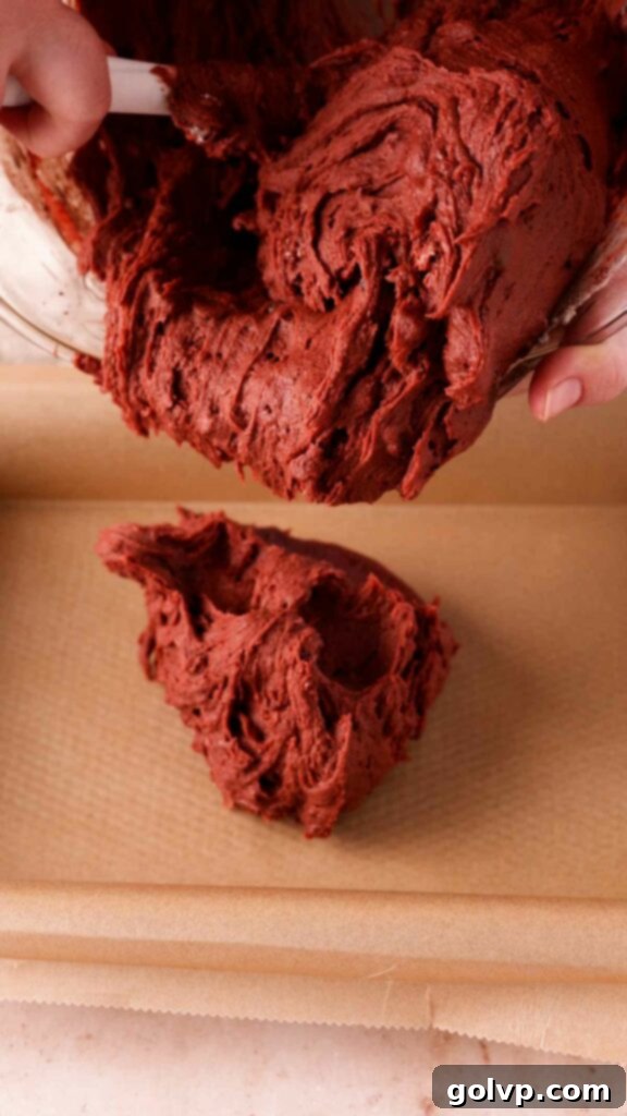 Adding rich red velvet brownie batter into a prepared baking pan.
