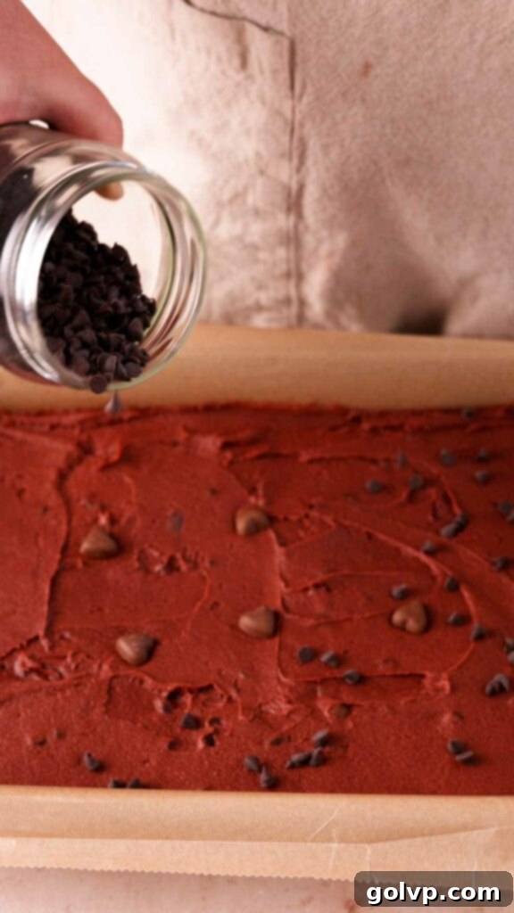 Topping the red velvet brownie batter with extra chocolate chips before baking.
