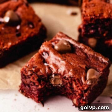 A deliciously fudgy red velvet brownie with a bite taken out, revealing a rich red interior and chocolate chips, adorned with small chocolate hearts for a festive touch.