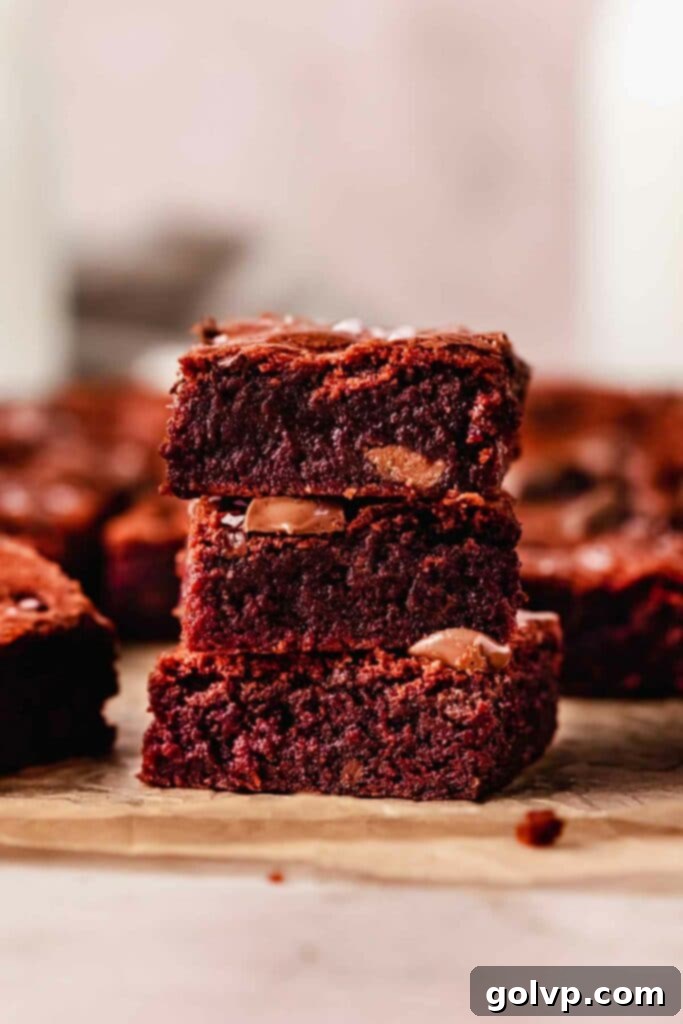 A stack of three incredibly fudgy red velvet brownies, showcasing their rich red color and dense texture.