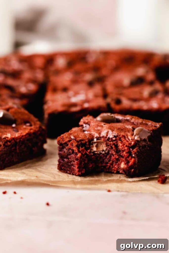 A close-up of a bitten red velvet brownie, showing its moist, fudgy interior and melted chocolate chips.