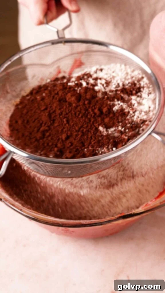 Sifting cocoa powder and flour into the wet brownie batter for a smooth consistency.