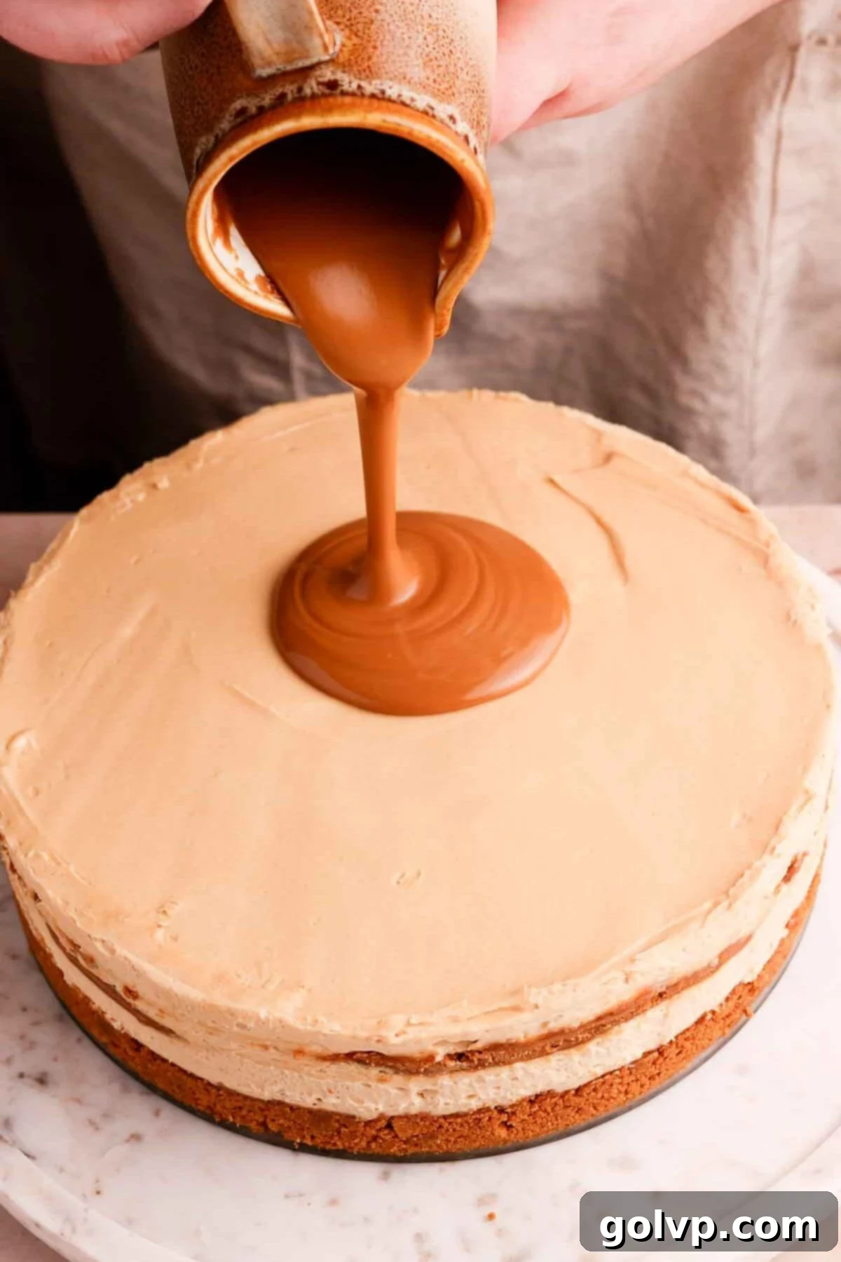 Pouring a luxurious melted Biscoff drip over the chilled cheesecake.