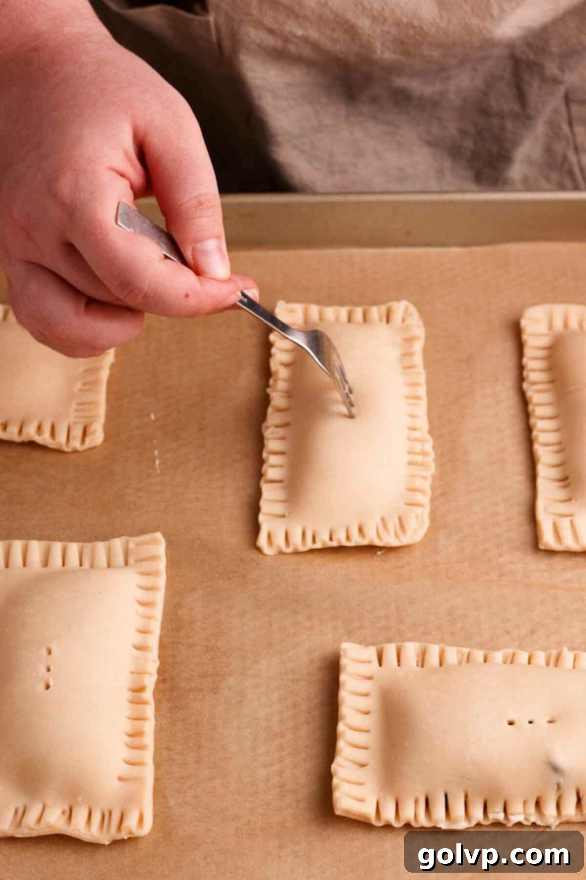 Crimping the edges of the pop tarts with a fork for a secure seal and poking holes for venting.