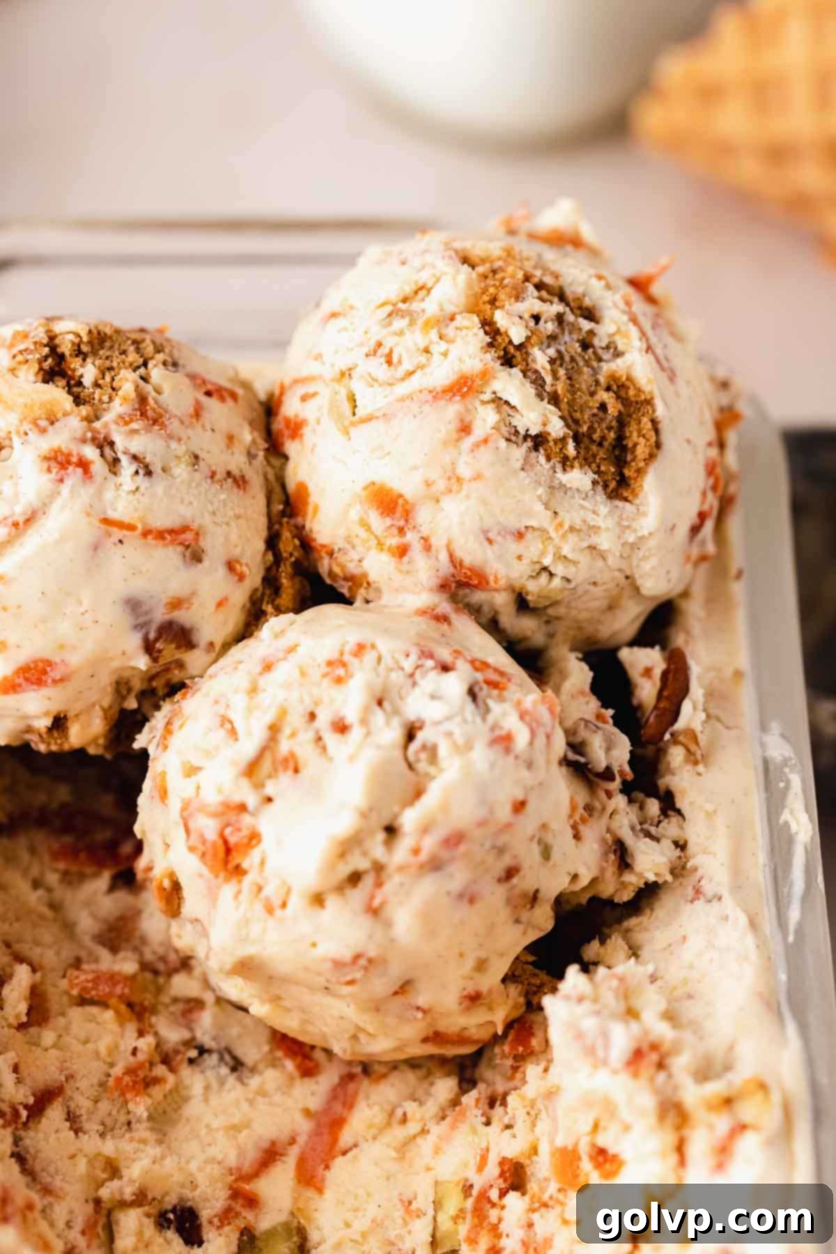 Spiced Carrot Cake Swirl 2 scooped creamy carrot cake ice cream in a white bowl, garnished with pecans and cookie crumbs