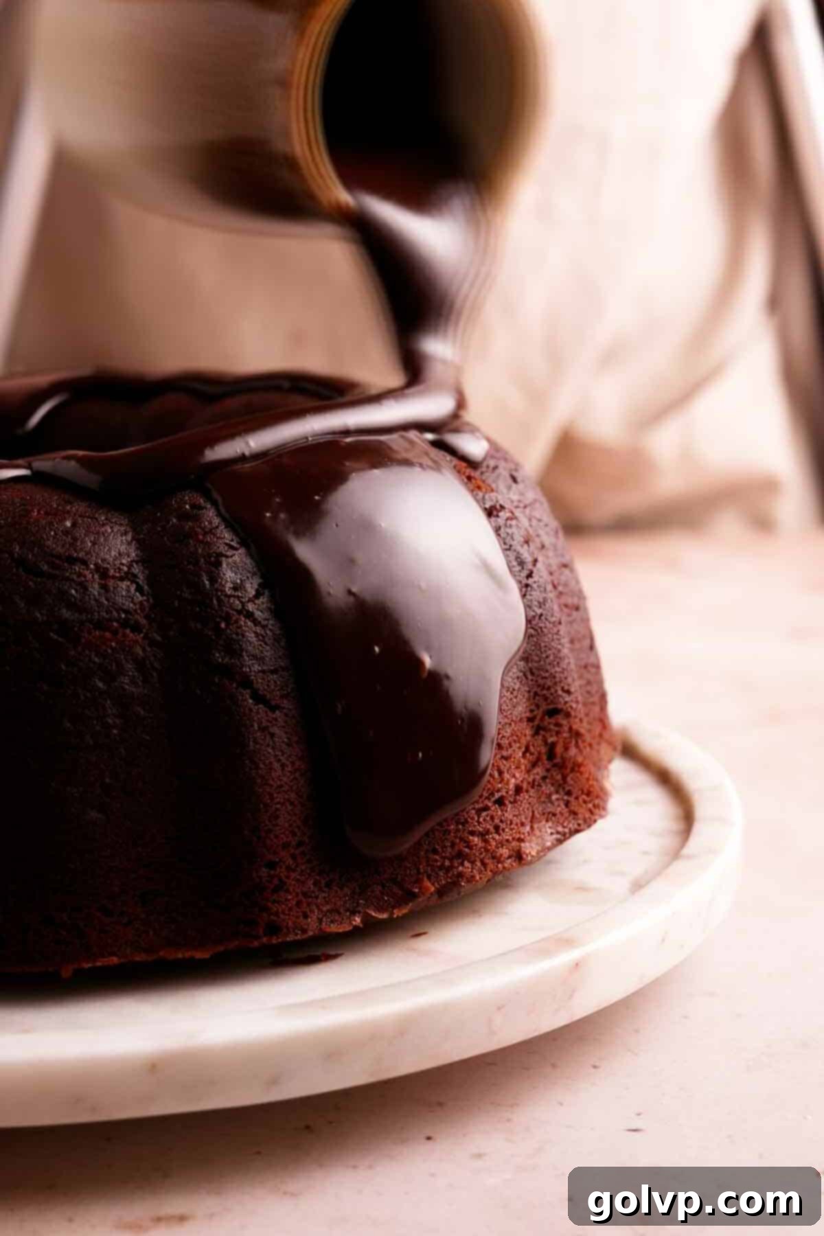 Pouring chocolate ganache glaze on top of a bundt cake.