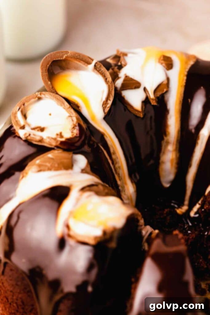Full view of a chocolate Cadbury creme egg bundt cake with broken creme eggs on top, glistening with milk chocolate glaze.