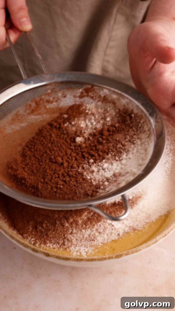 Sifting dry ingredients into the wet batter for a chocolate bundt cake.
