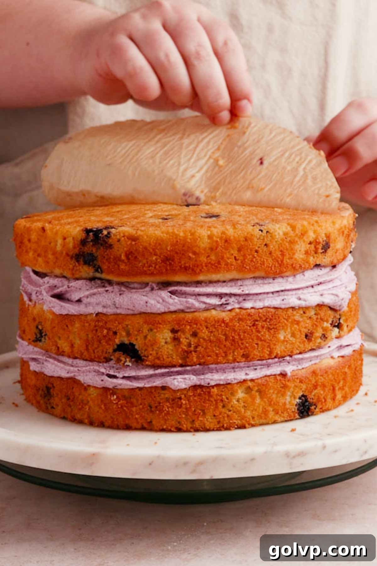 stacked cake layers with filling and peeling off the parchment paper off the bottom of the top layer