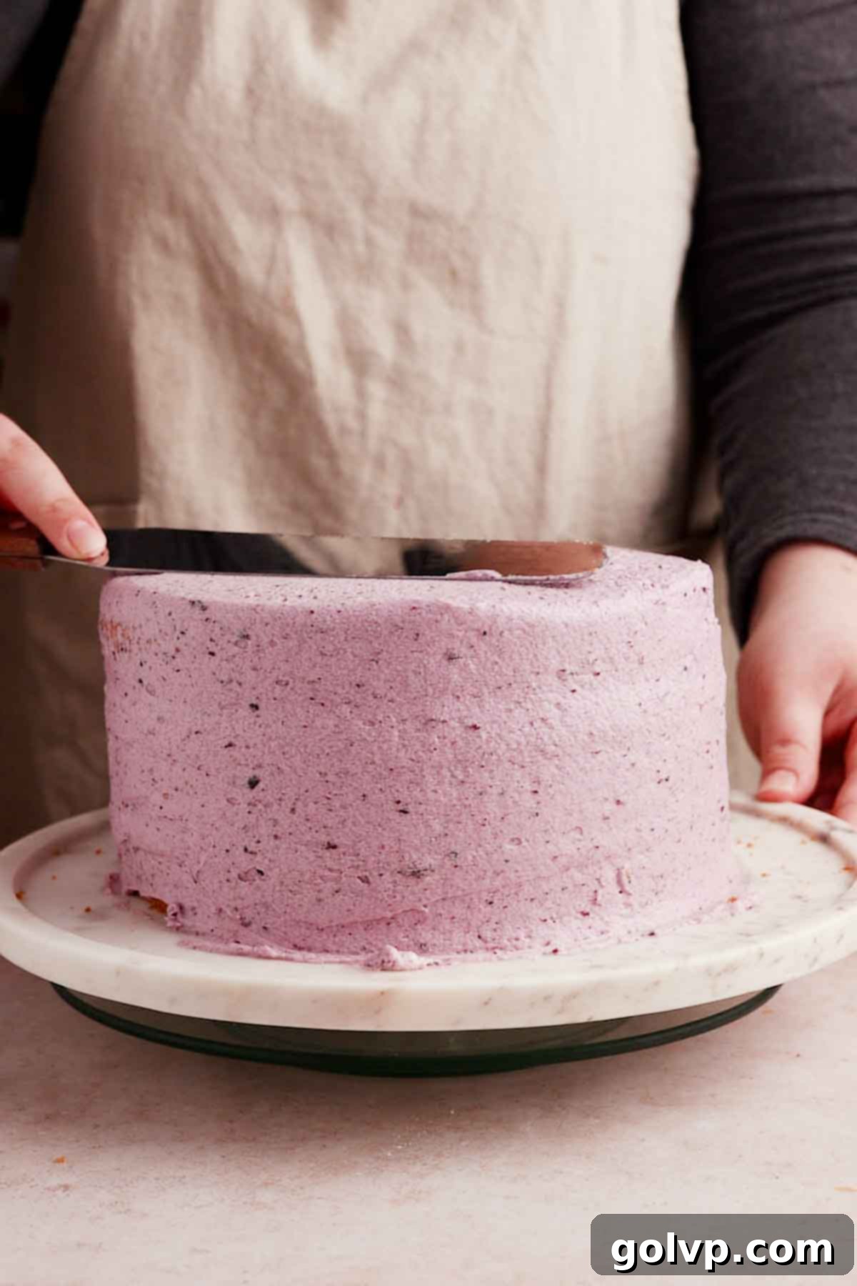 smoothing frosting on blueberry birthday cake with a long metal spatula