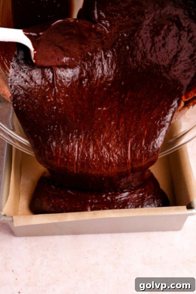 Pouring the rich brownie batter into a parchment-lined baking pan