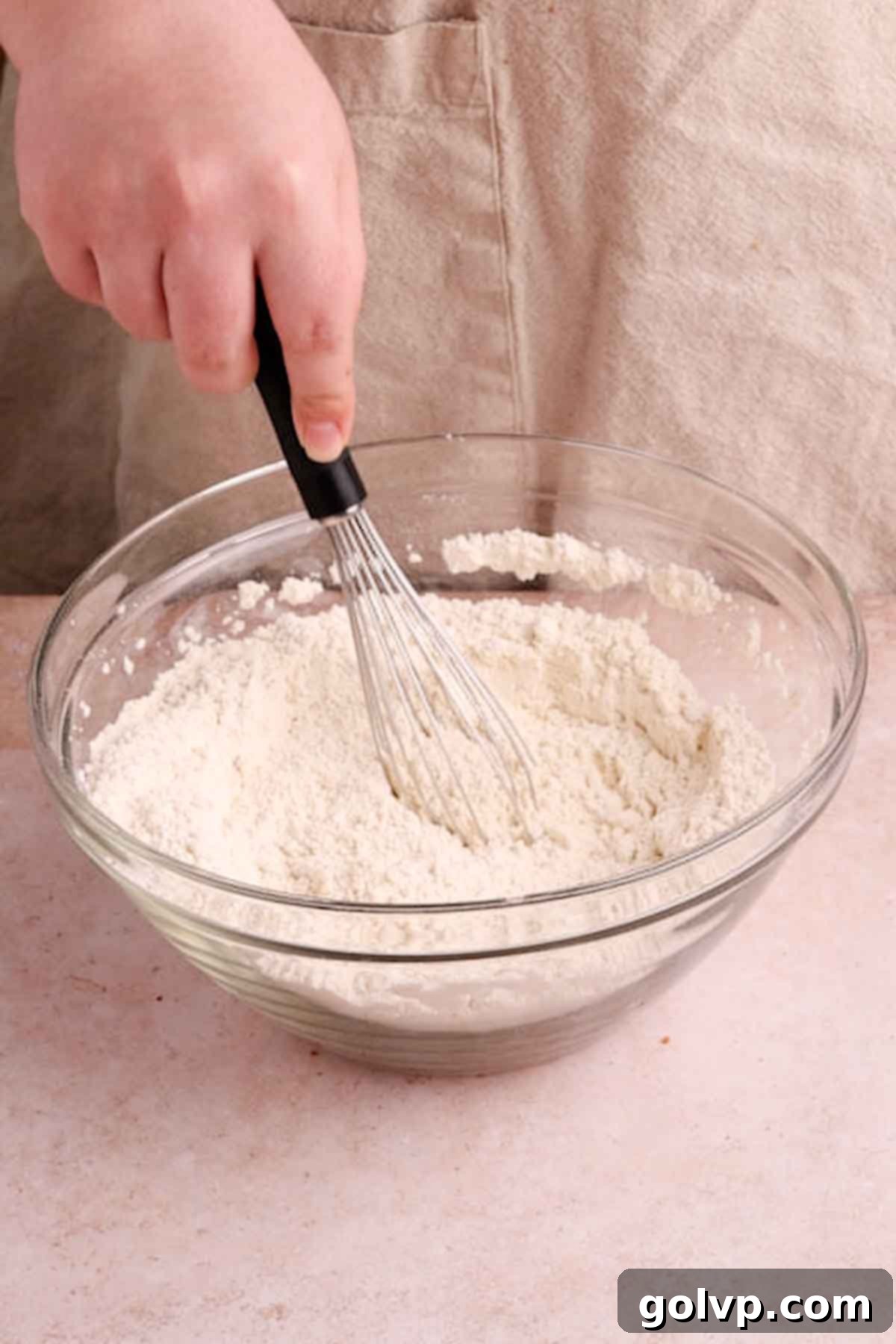 A large mixing bowl containing sifted dry ingredients for Biscoff cookies, including flour, cornstarch, baking powder, baking soda, and cinnamon, with some crushed Biscoff crumbs visible.
