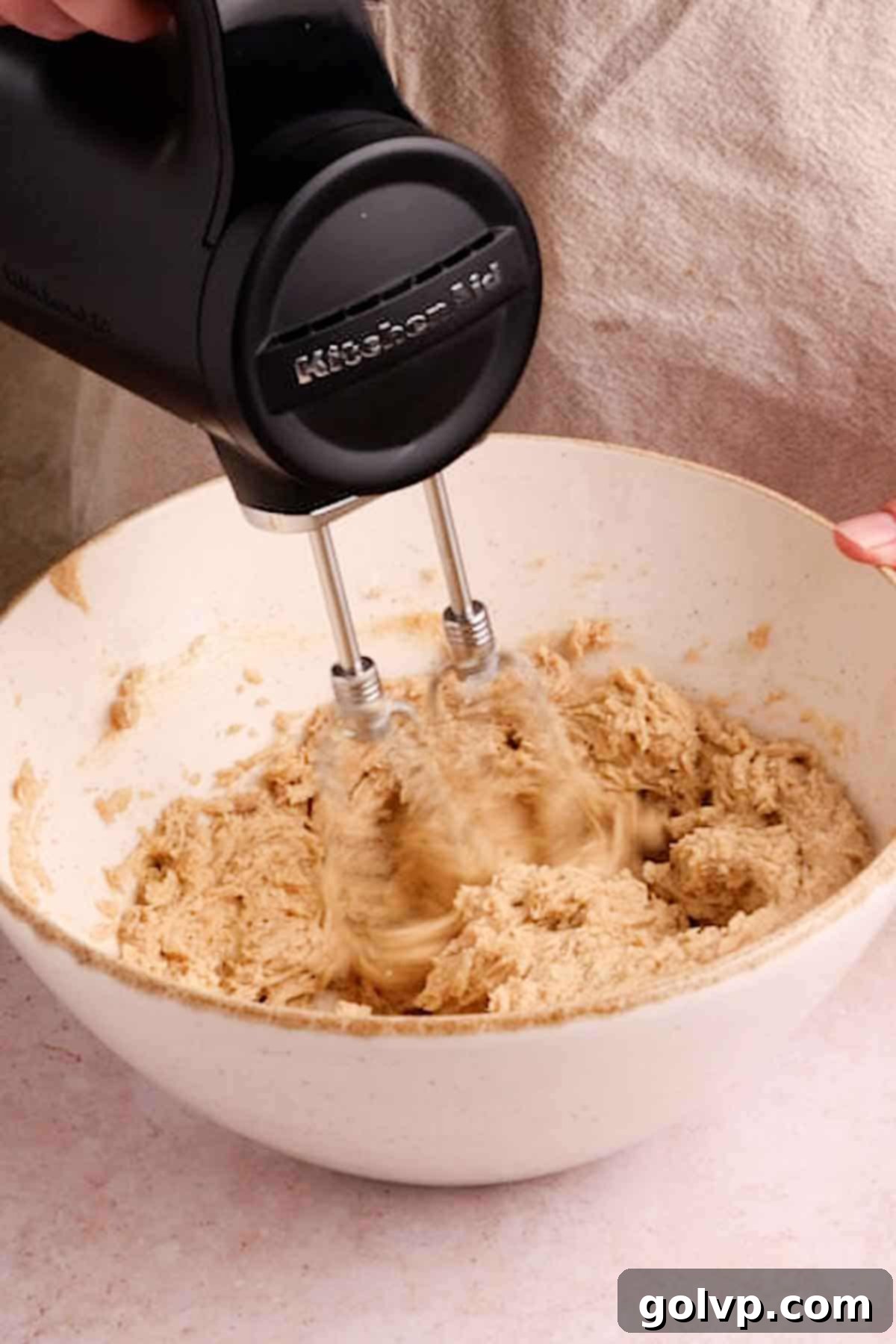 An electric stand mixer actively beating softened butter, brown sugar, and granulated sugar in a large bowl, creating a light and fluffy mixture.