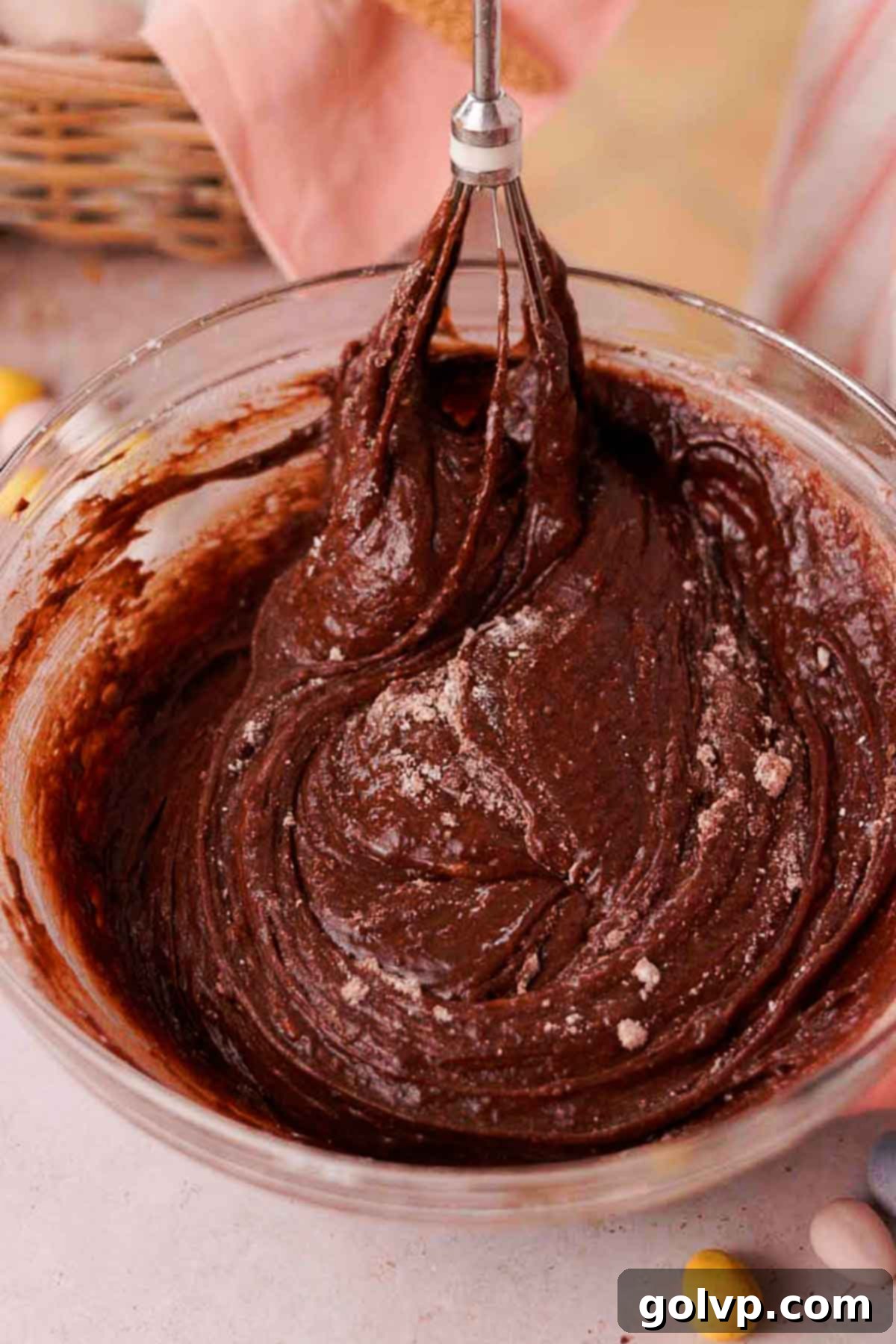 folding flour and cocoa powder into brownie batter with a whisk in a glass bowl