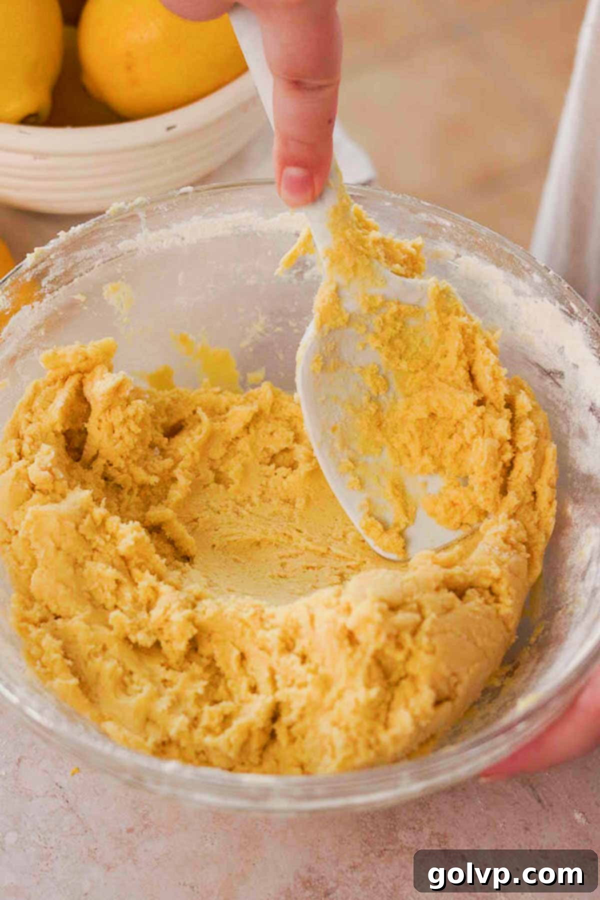 Gently stirring the cookie dough for lemon cookies in a glass bowl with a silicone spatula after adding dry ingredients