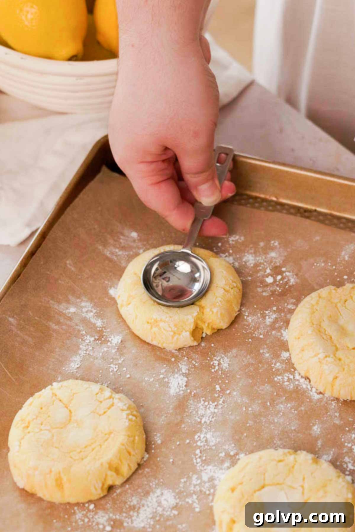 Using the back of a spoon to deepen the indents in freshly baked lemon cookies on a parchment-lined tray