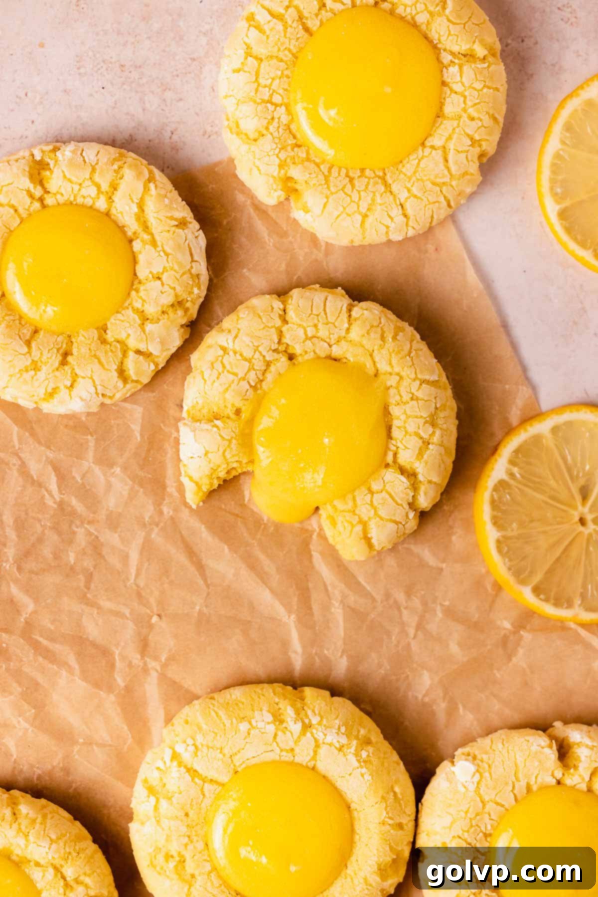 Beautifully arranged lemon curd filled cookies on parchment paper, garnished with fresh lemon slices, showcasing their vibrant color and crinkled tops
