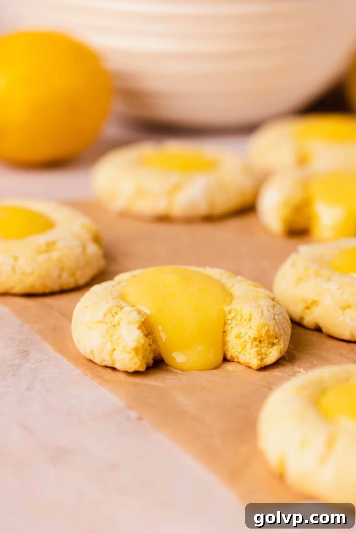 A stack of lemon curd filled cookies on parchment paper, with a generous amount of curd oozing out, emphasizing the rich filling