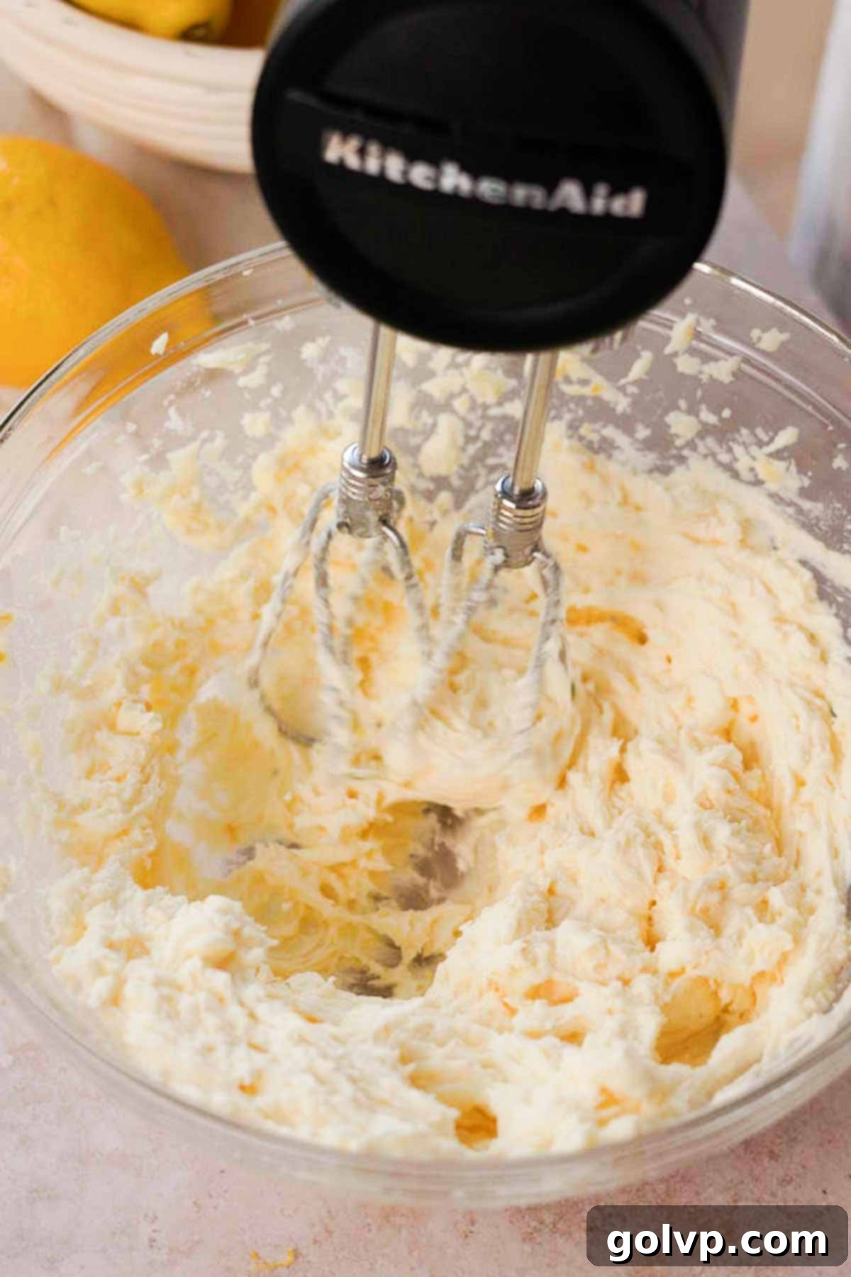 Beating lemon-infused sugar, softened butter, and cream cheese in a large glass bowl with an electric mixer until light and creamy