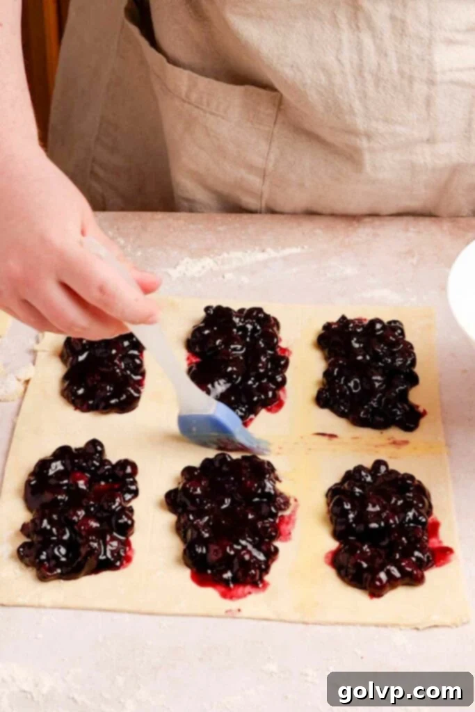 Filling pastry with blueberry filling and brushing with egg wash before covering