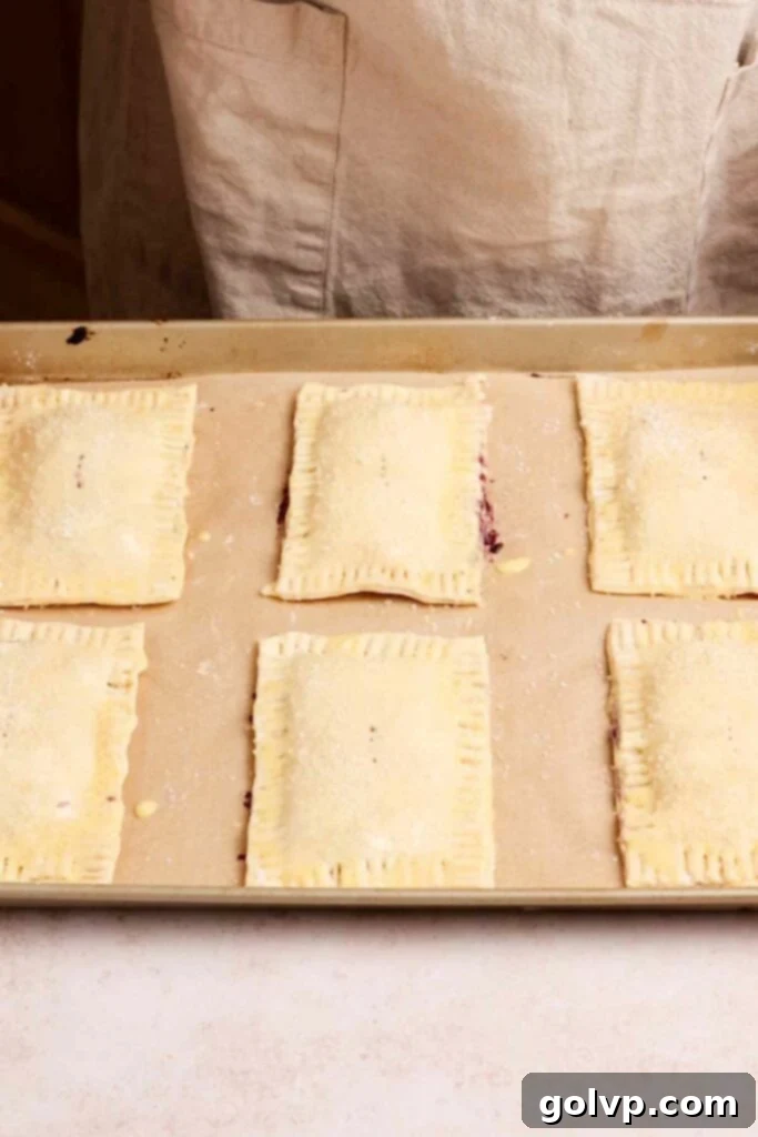 Unbaked blueberry pop tarts with crimped edges and coarse sugar on a baking tray