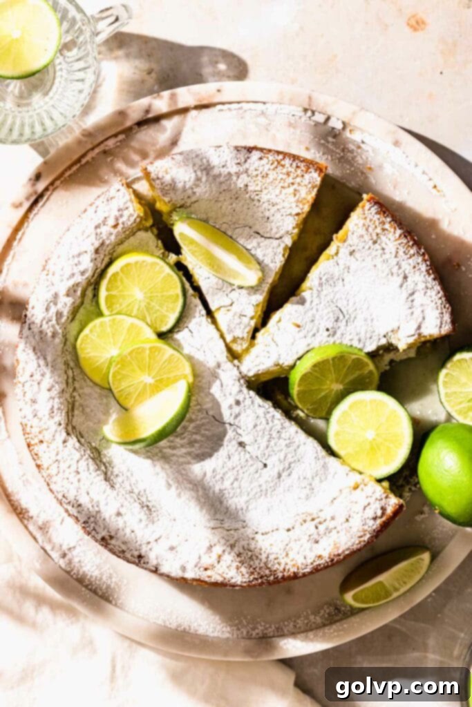 Sliced lime cake topped with powdered sugar and fresh lime slices, showing the gooey filling.