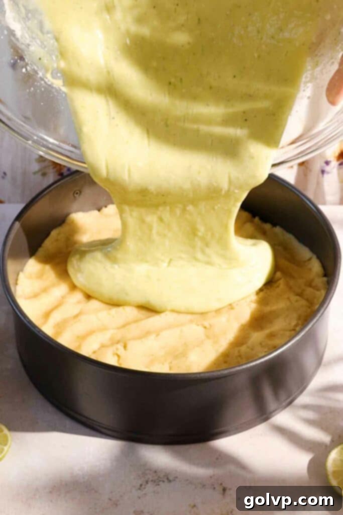 Pouring the creamy lime filling onto the prepared cake batter in a baking pan.