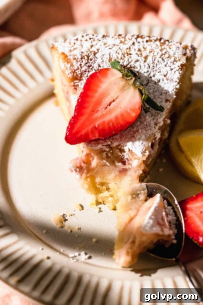 A slice of strawberry butter cake with a fresh strawberry on top, showing the gooey filling and buttery crust.