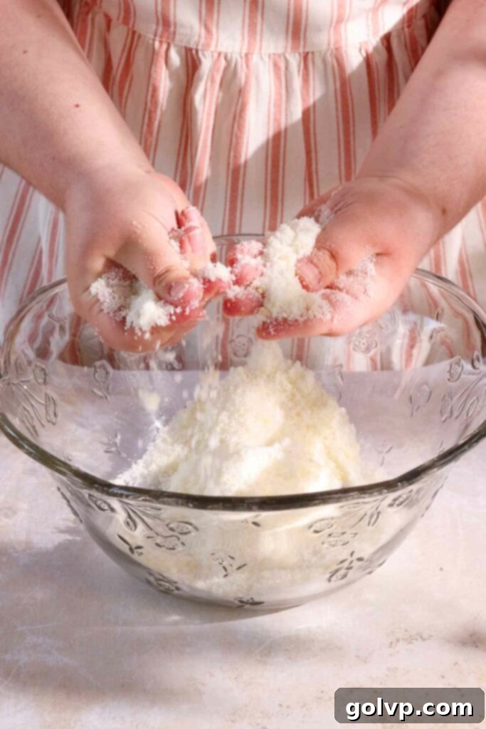 Hands rubbing lemon zest and sugar together in a bowl to release fragrance.