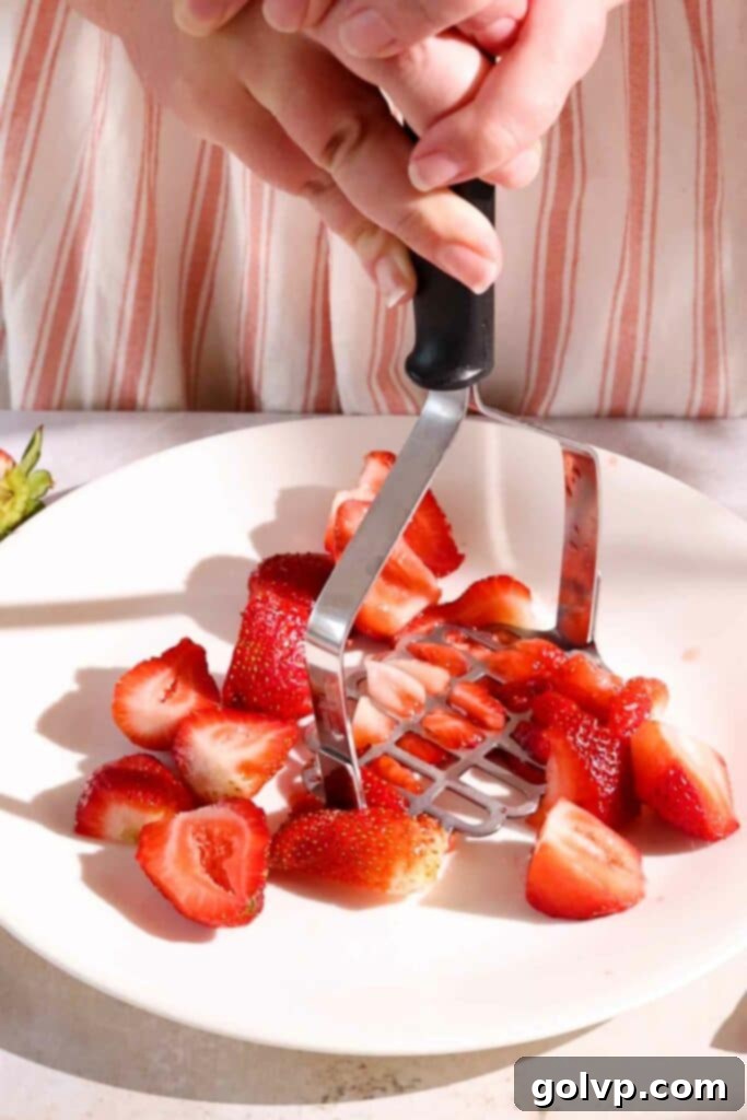 Mashing fresh strawberries with a potato masher for the gooey filling.