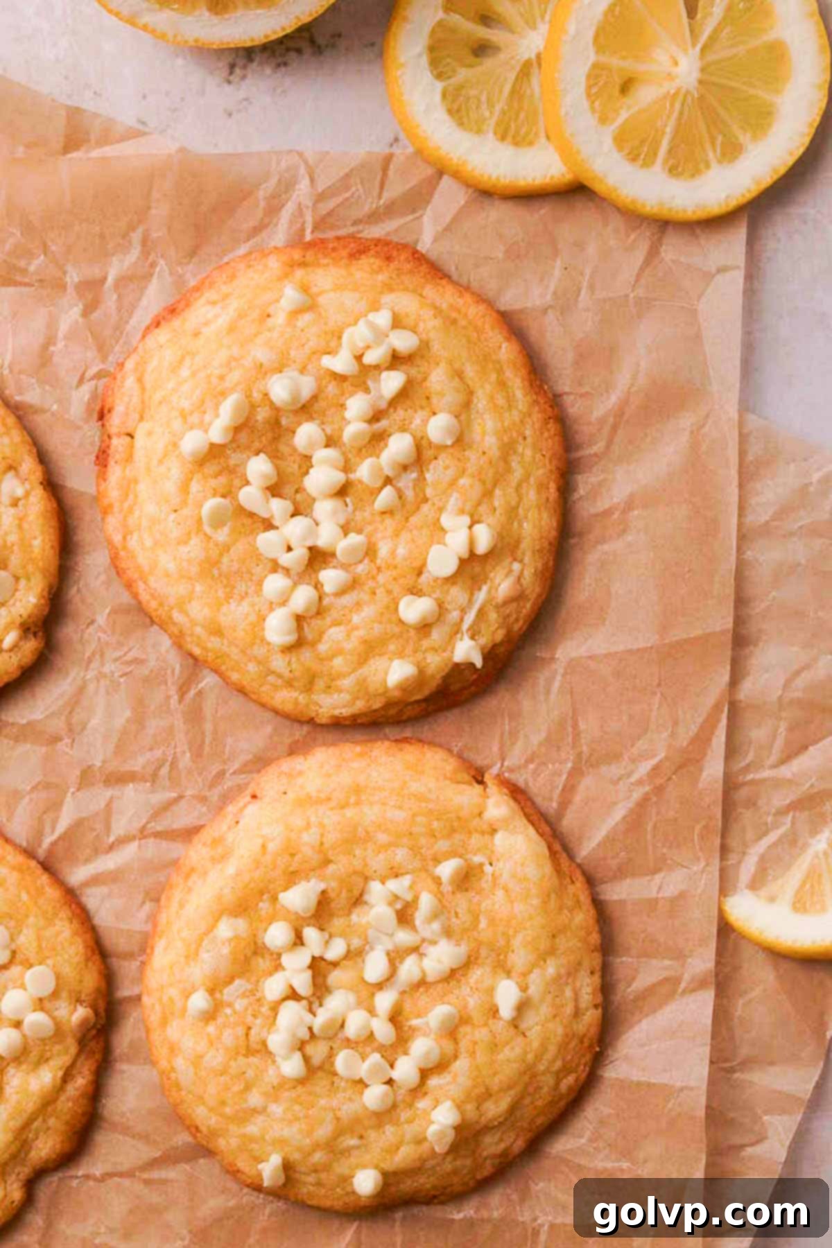 Freshly baked lemon white chocolate cookies cooling on parchment paper on a baking tray, their golden edges visible.