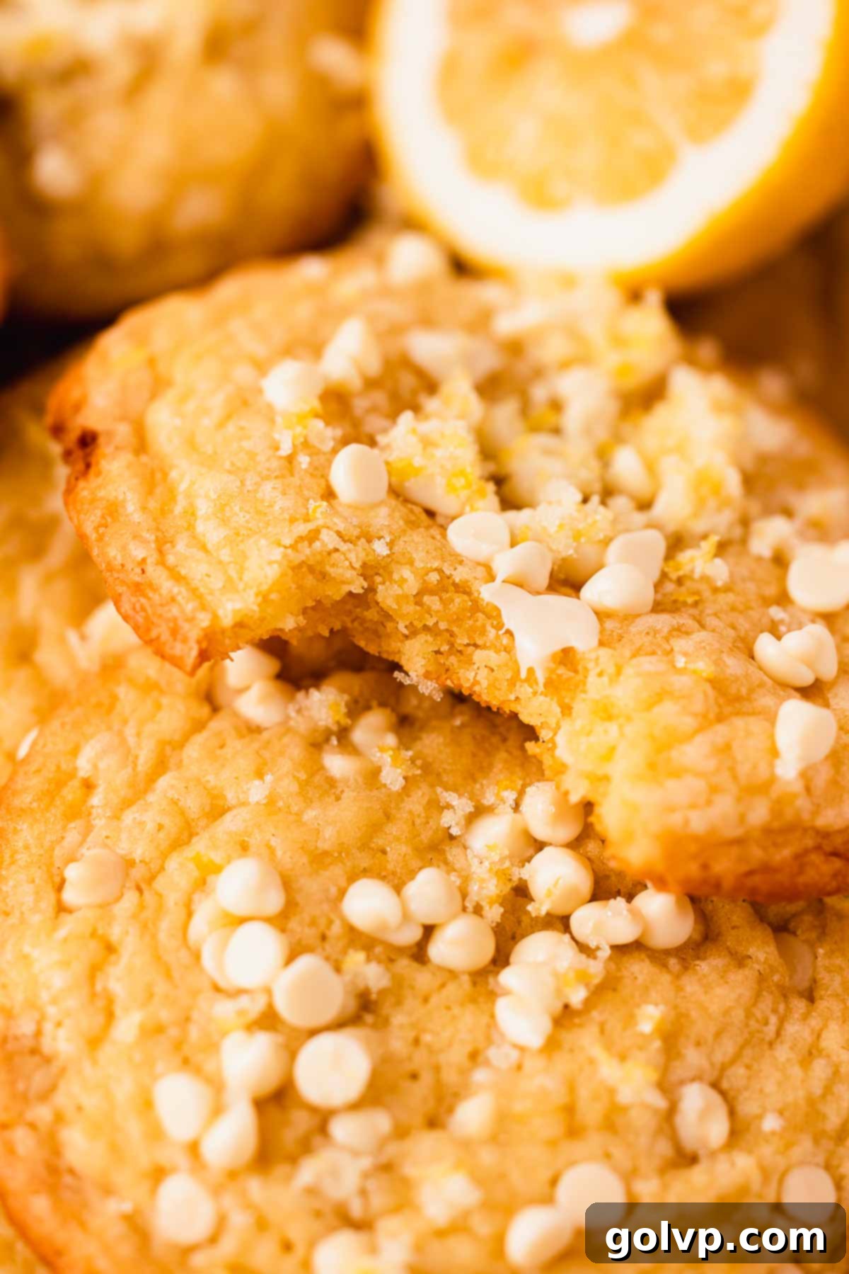 A close-up of a bitten lemon white chocolate cookie, revealing its soft, chewy interior studded with melted white chocolate pieces.