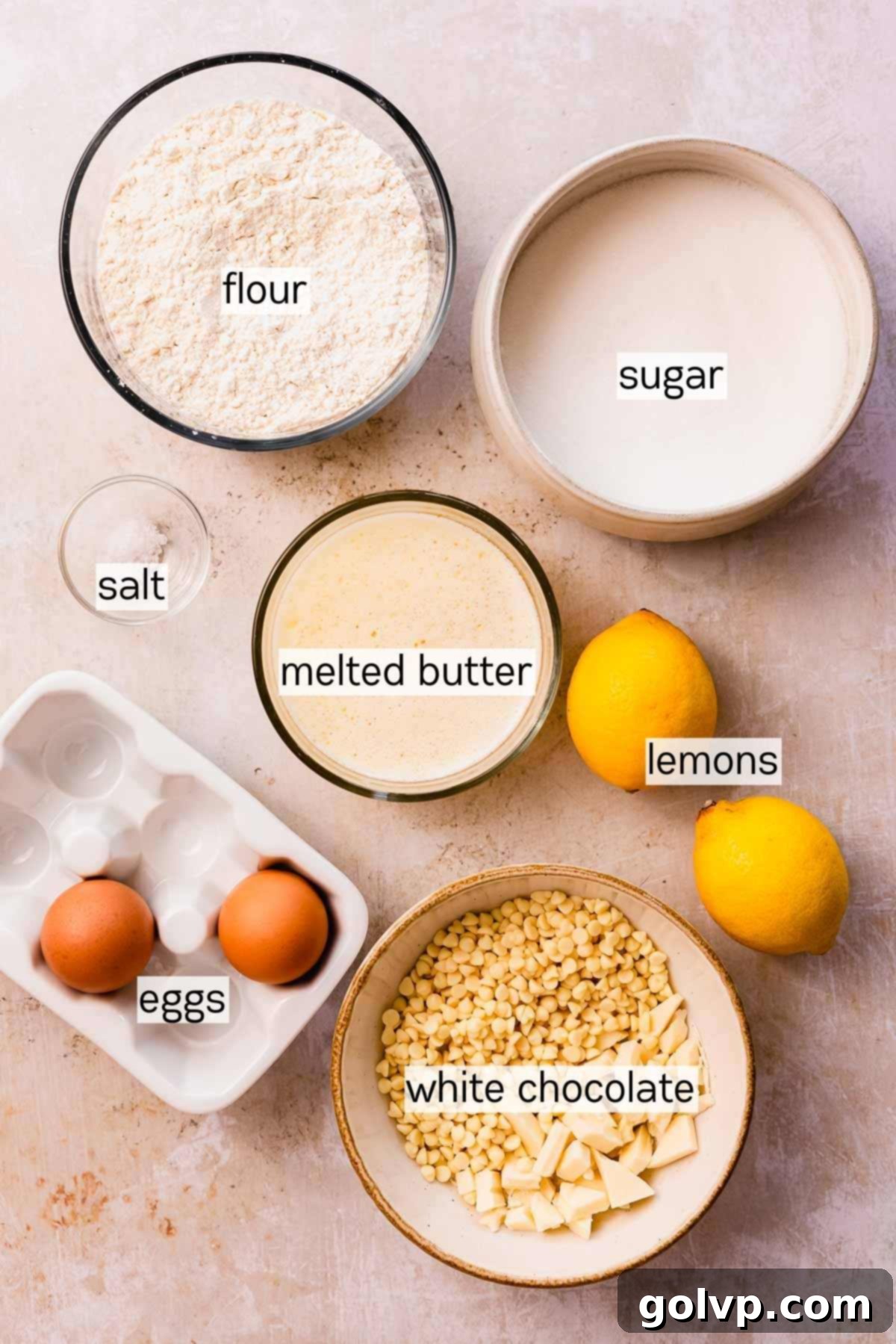 Individual bowls containing all the fresh and measured ingredients for lemon white chocolate cookies: lemons, butter, white chocolate, flour, sugar, and eggs.