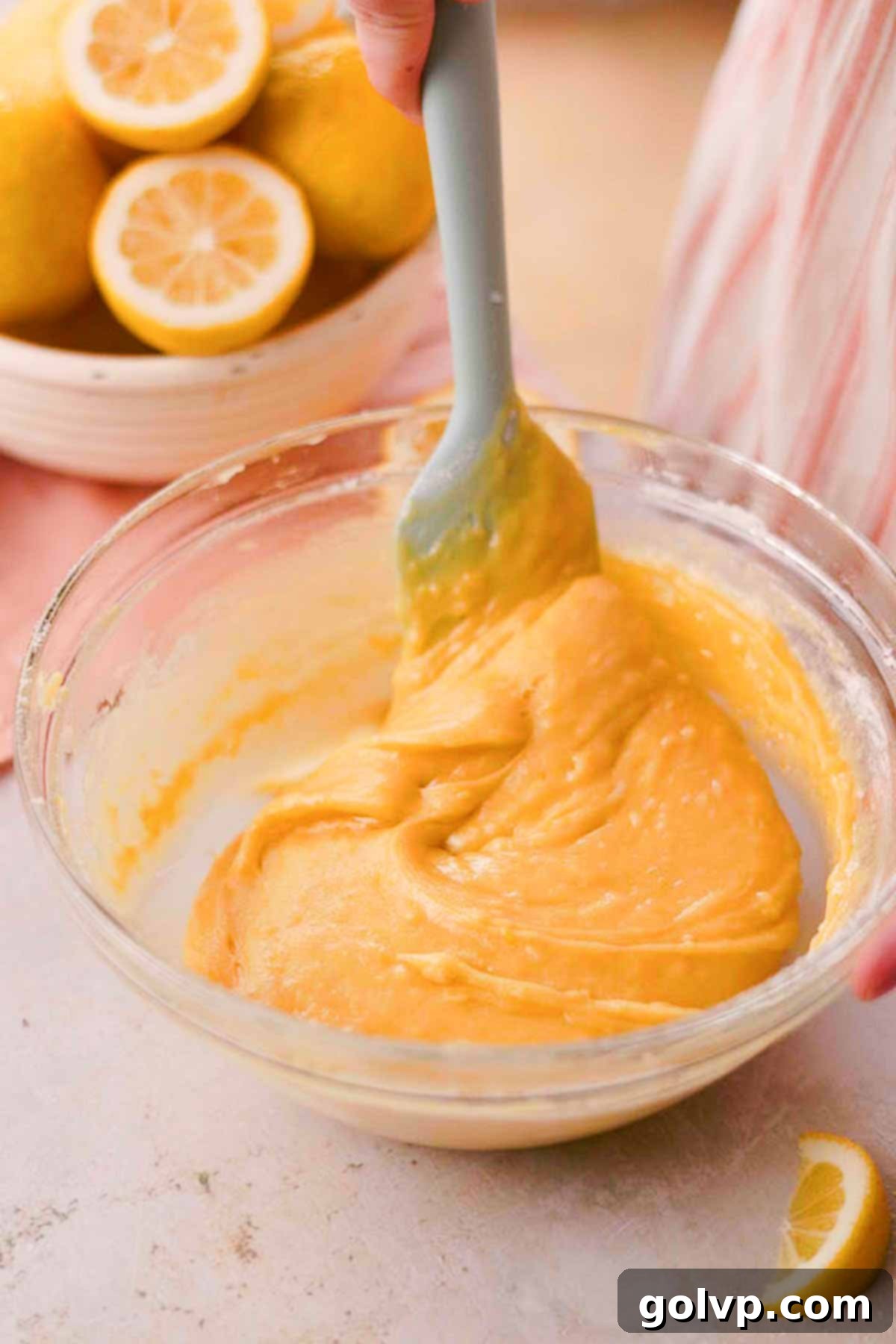 A spatula gently folding all-purpose flour and baking soda into the lemon cookie dough in a large glass bowl until just combined.