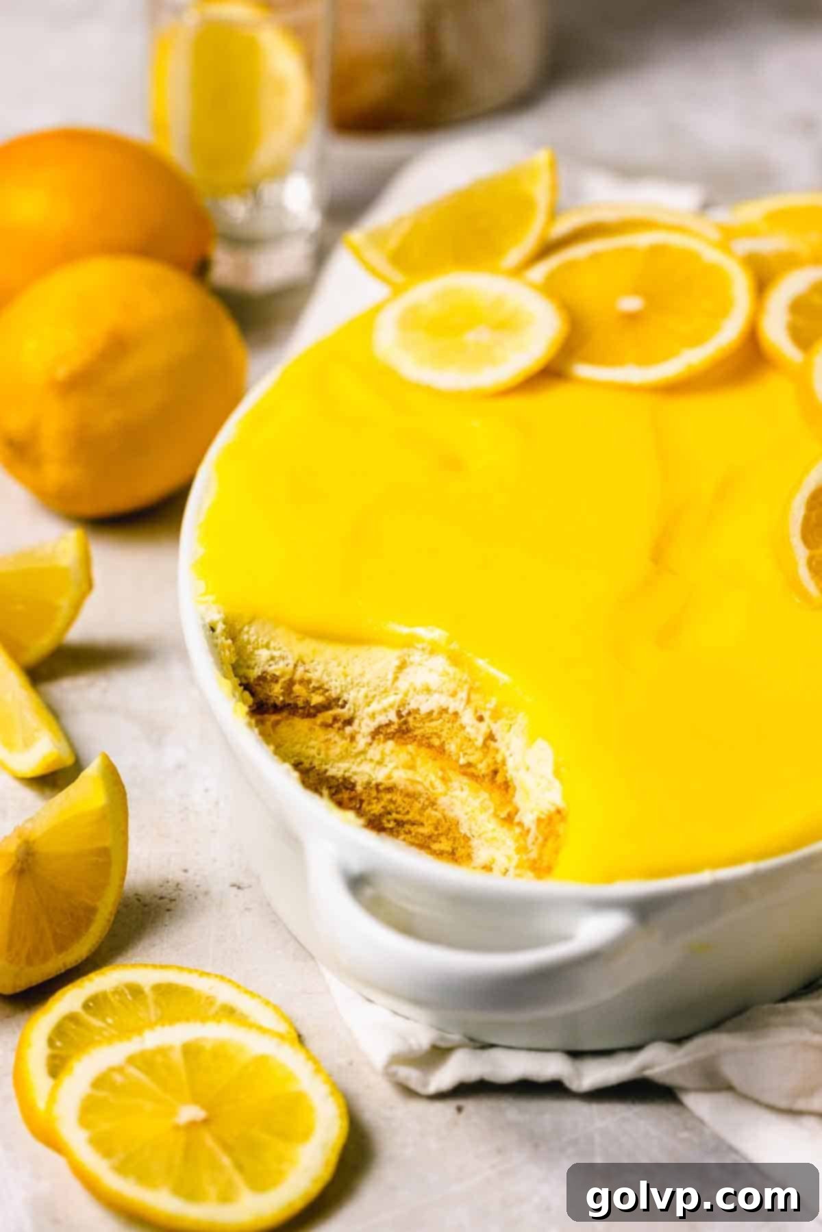 lemon tiramisu in white dish with handles and a scoop taken out to show two layers of ladyfingers in creamy filling