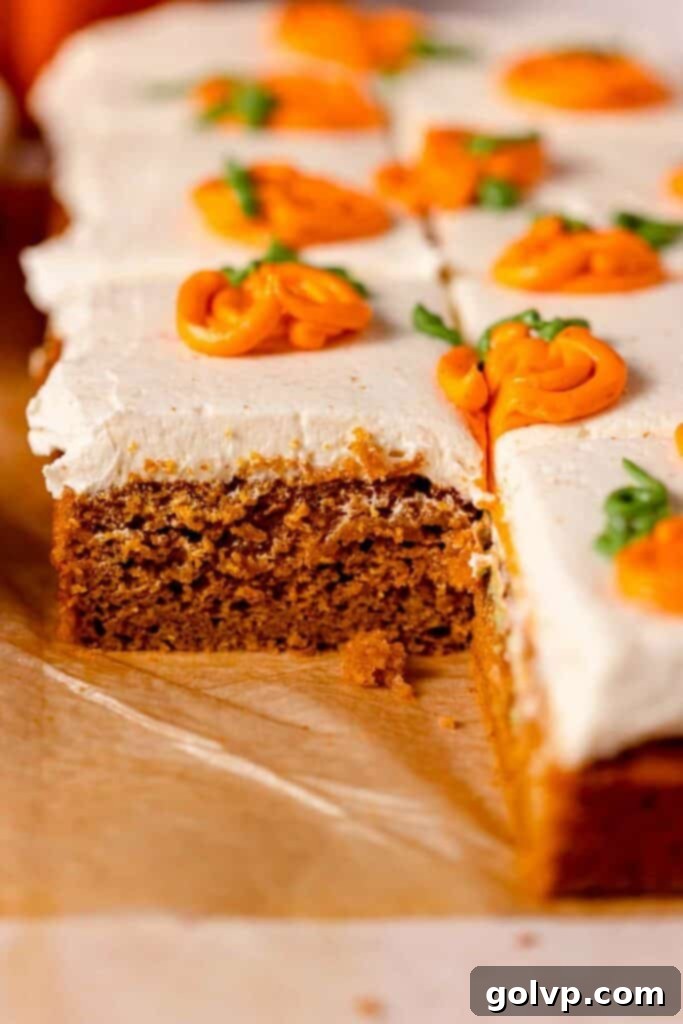 Rustic pumpkin cake on parchment paper, beautifully frosted with white cream cheese frosting and adorned with cheerful orange piped pumpkins, ready for a fall celebration.
