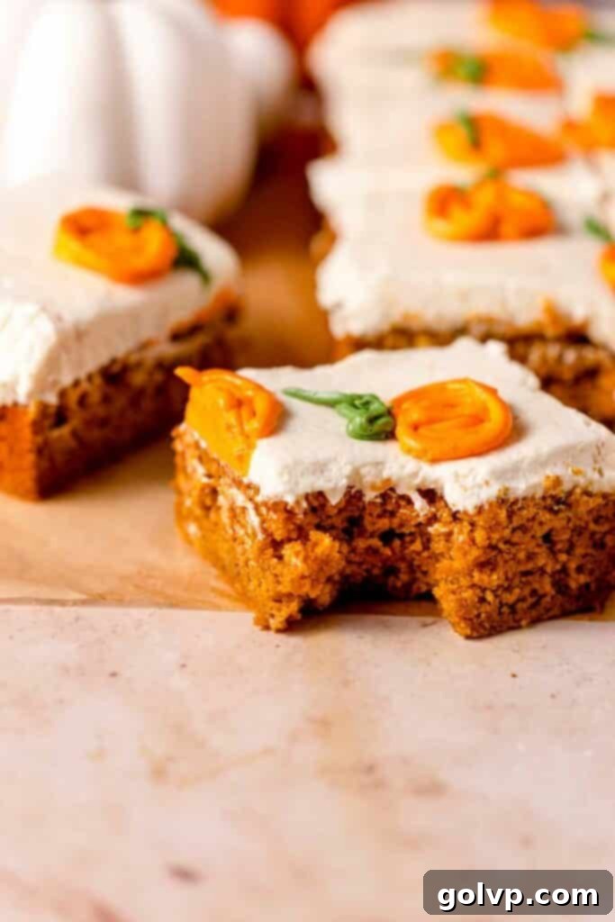 A slice of pumpkin cake with a bite taken, revealing the tender crumb, topped with smooth white frosting and charming piped pumpkin decorations.